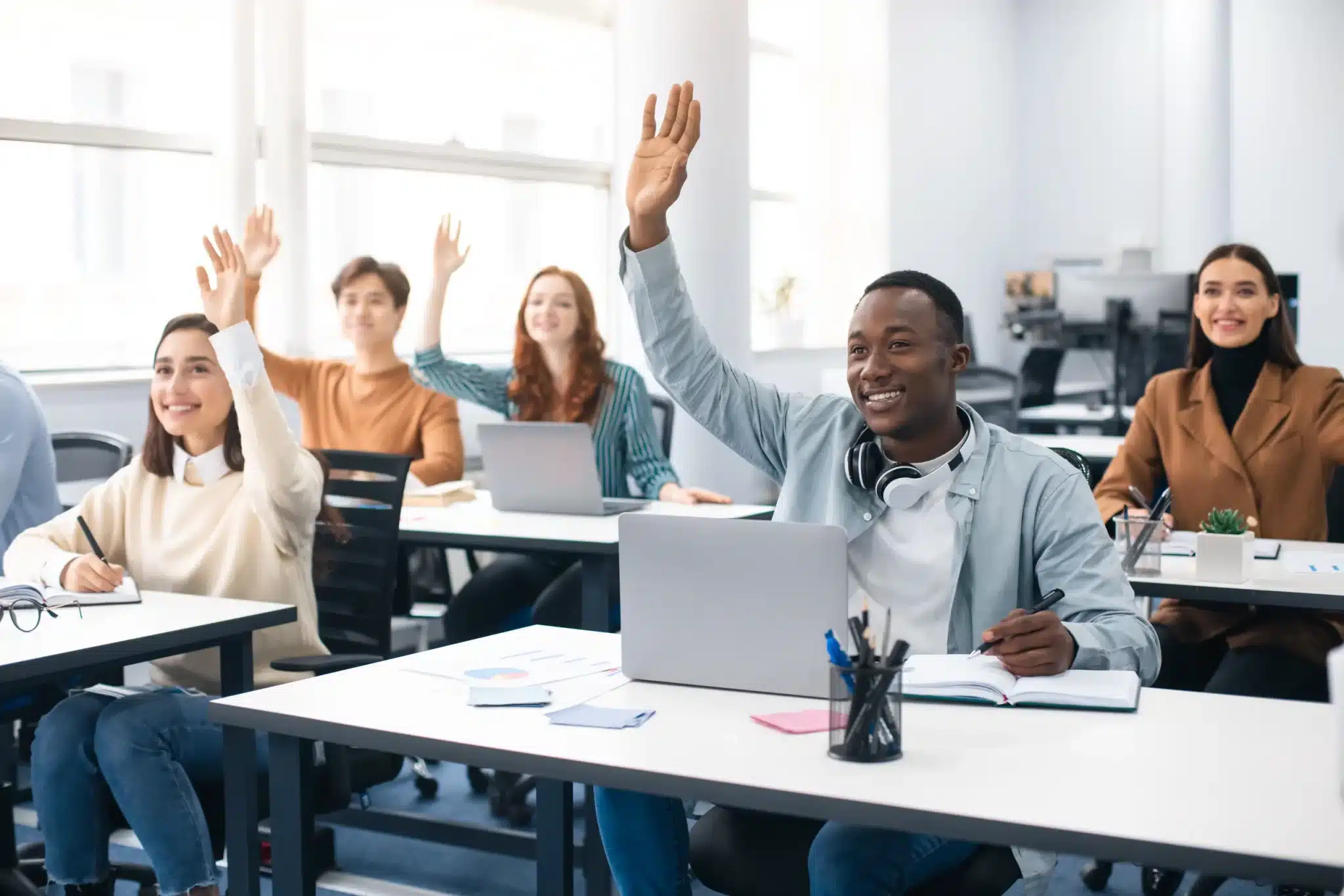 Diverse group of professionals participating in a corporate Czech language training class, raising hands during a lesson.