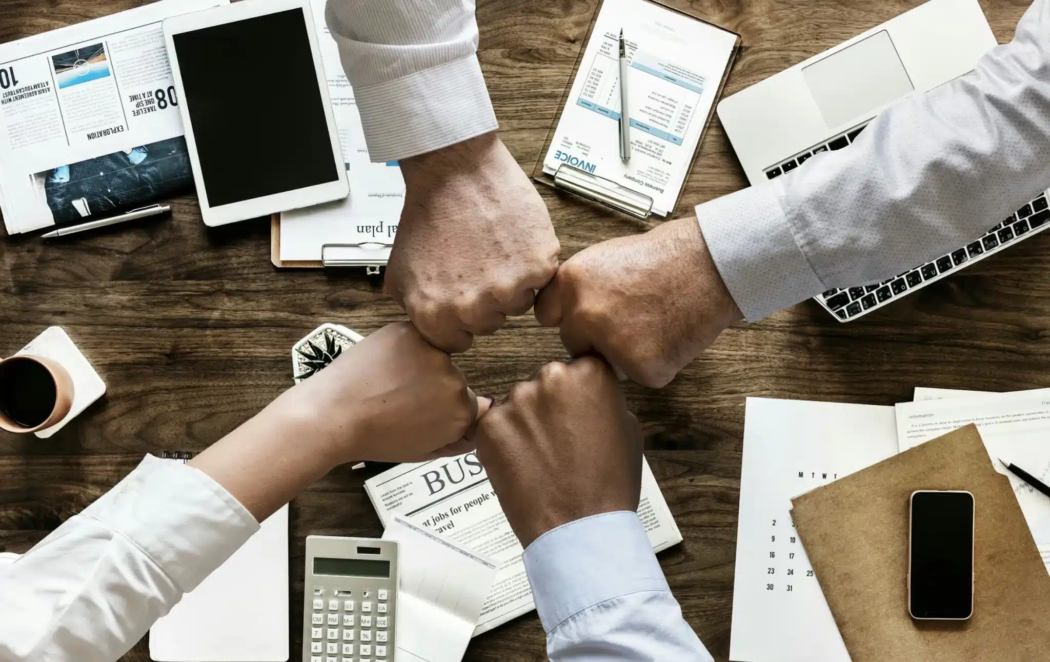 Four individuals engaging in a fist bump over a business meeting table, symbolizing teamwork and collaboration in corporate Czech training.